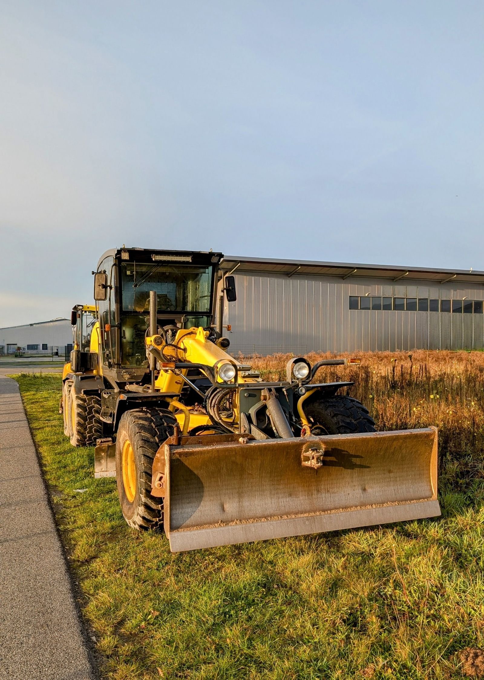 Motor grader parked beside an industrial warehouse in morning light